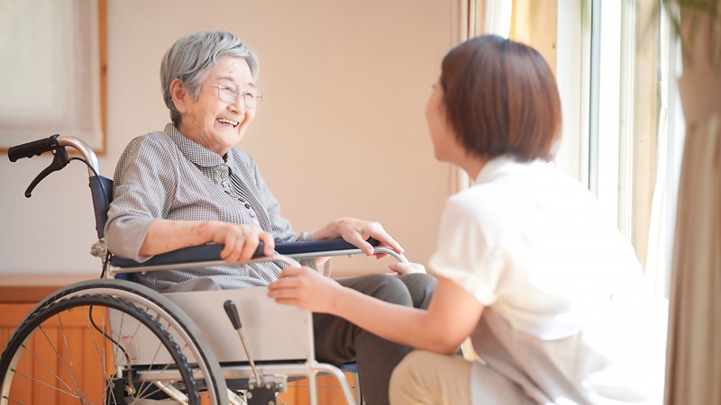 車いすの高齢女性に笑顔で話しかける介護士